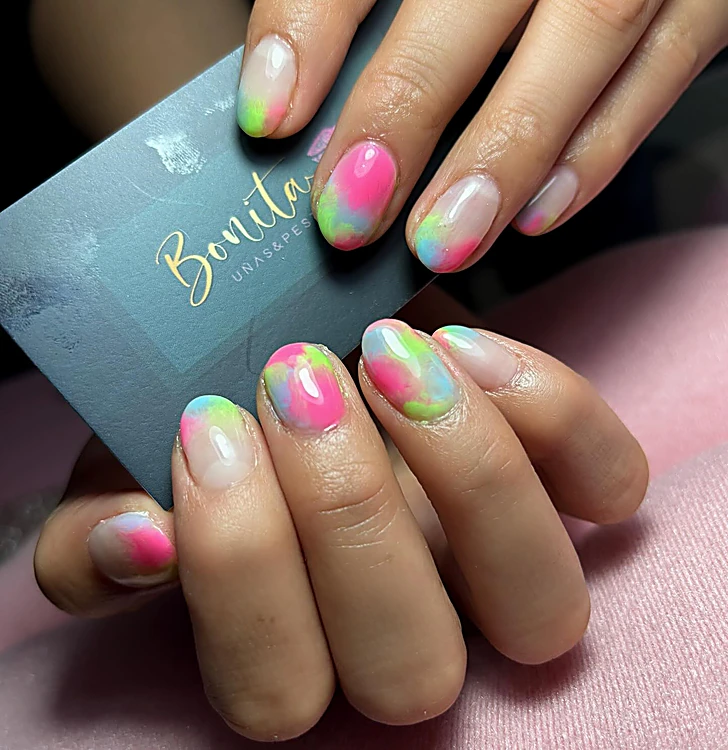 Uñas cortas con efecto aura en rosa, verde y azul, junto a la tarjeta de Bonita