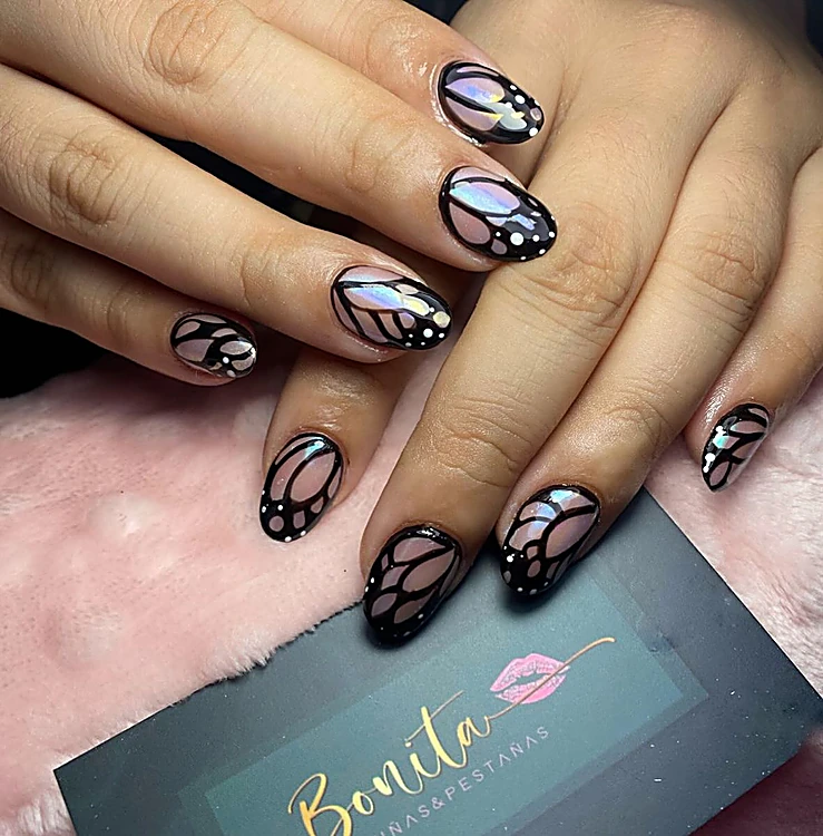 Uñas almendra con alas de mariposa negras y tornasol, junto a la tarjeta de Bonita