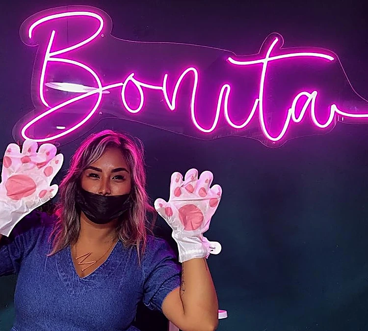 Integrante del equipo con guantes de gatito rosas bajo el letrero de neón magenta Bonita